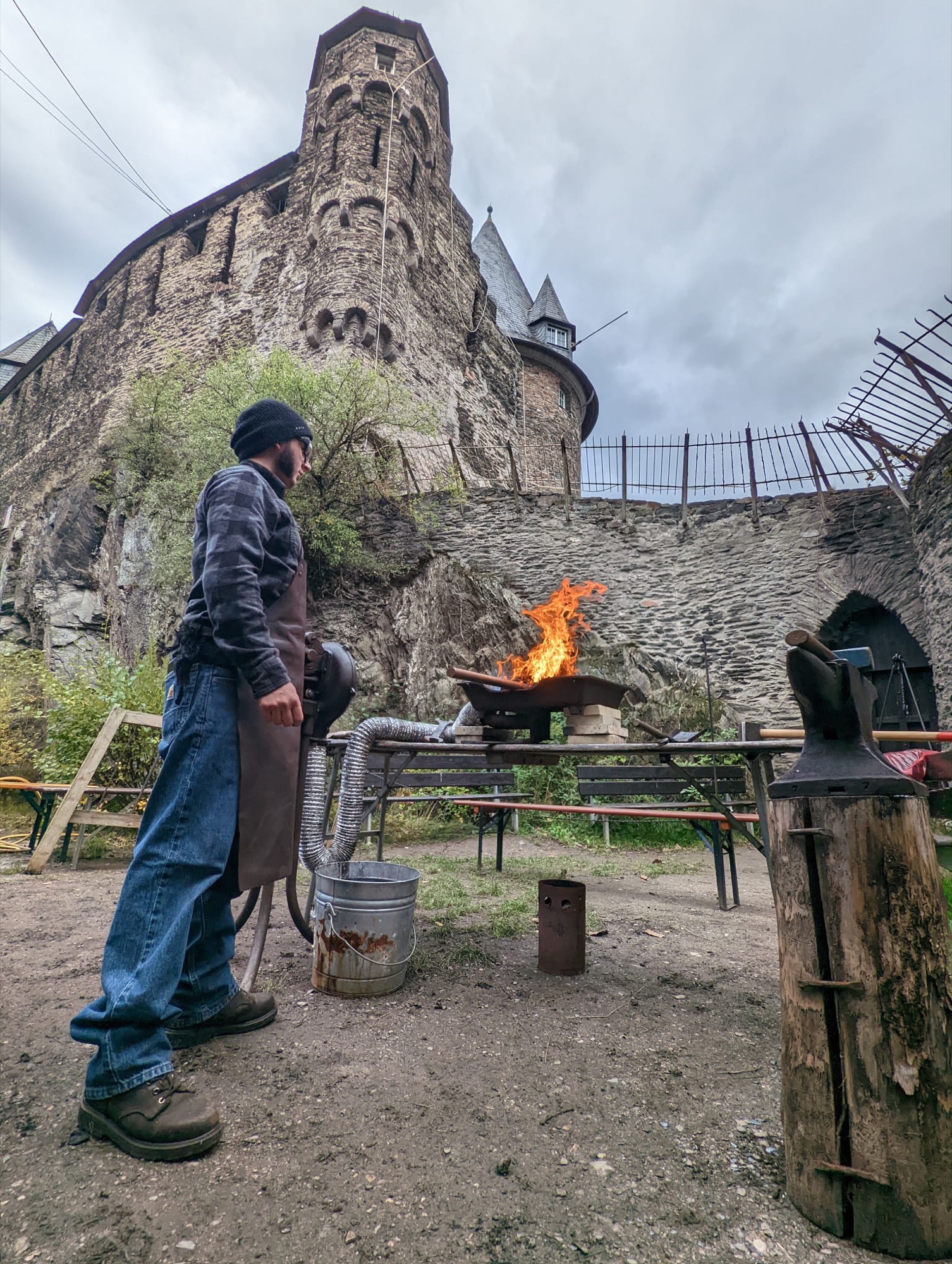 A blacksmith tending an outdoor forge beneath historic castle walls in Germany